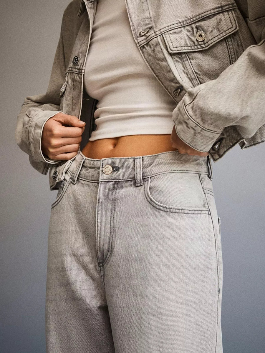 Person wearing a light gray jacket and jeans on a gray background