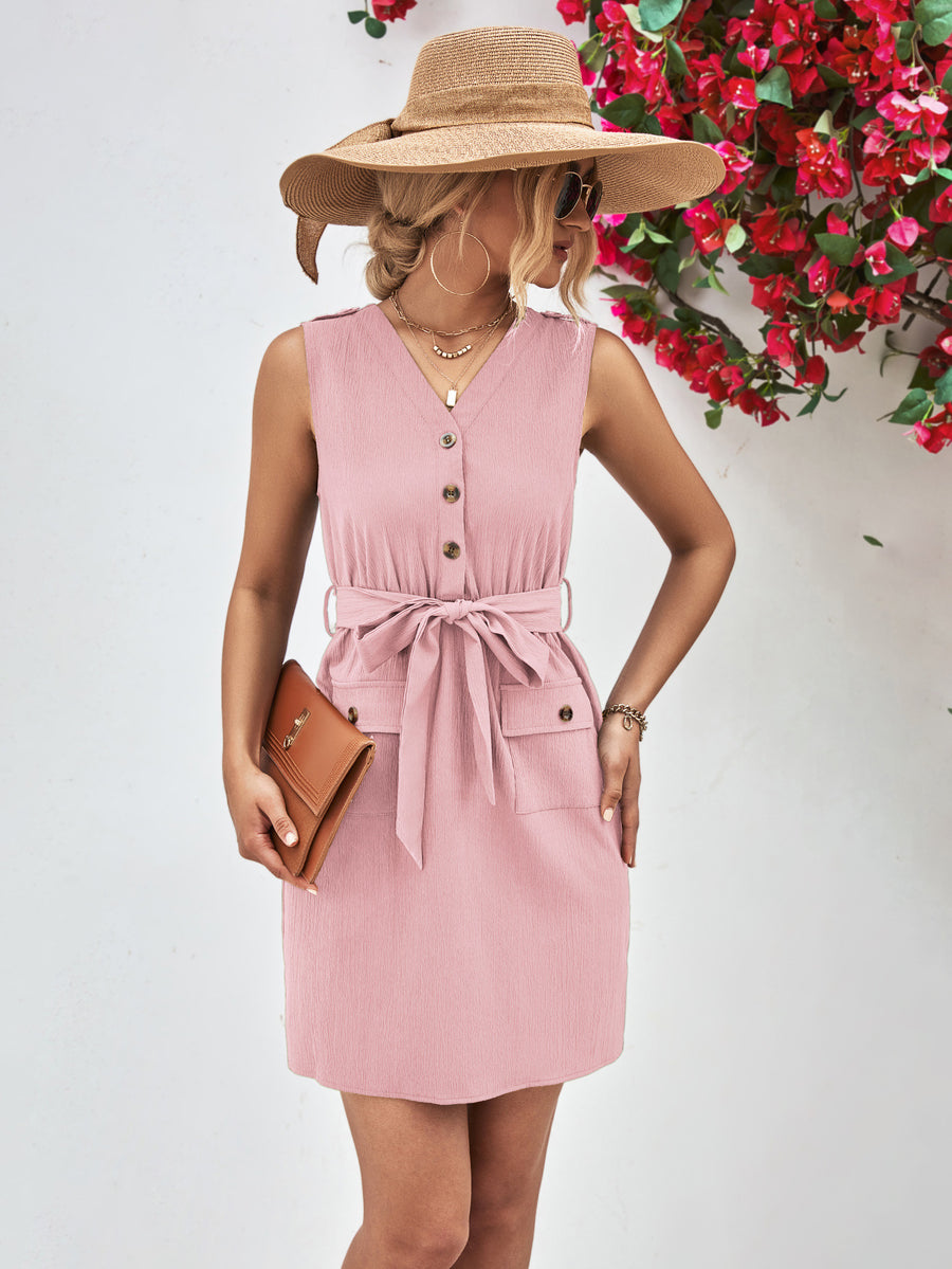 Woman wearing a pink dress with a wide-brimmed hat in front of red flowers.