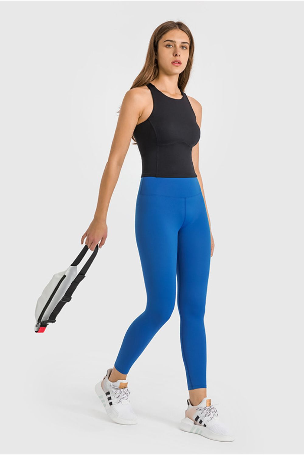 Woman wearing blue leggings and a black top, holding a tennis racket on a white background