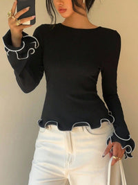 Person wearing a black long-sleeve top with white trim and white pants against a neutral background