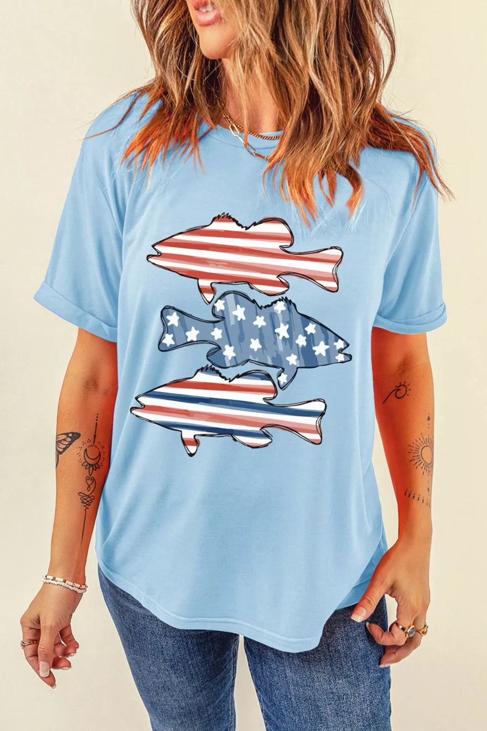 Woman wearing a light blue t-shirt with fish designs featuring the American flag on a beige background