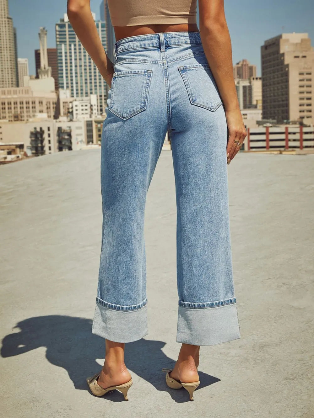 Person wearing light blue jeans on a rooftop with cityscape in the background