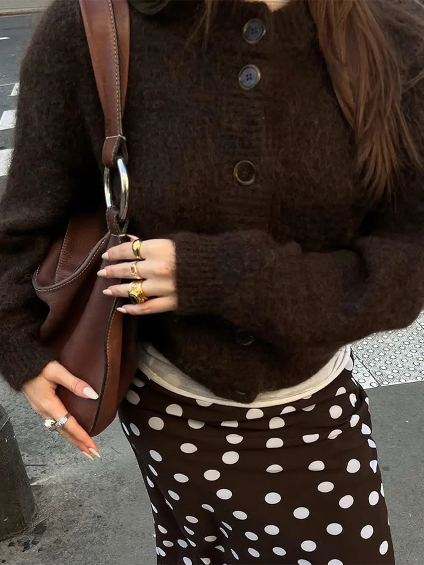 Person wearing a brown sweater and polka dot skirt holding a brown bag.