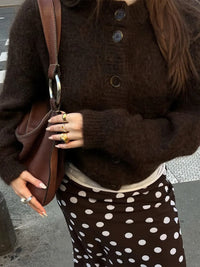 Person wearing a brown sweater and polka dot skirt holding a brown bag.