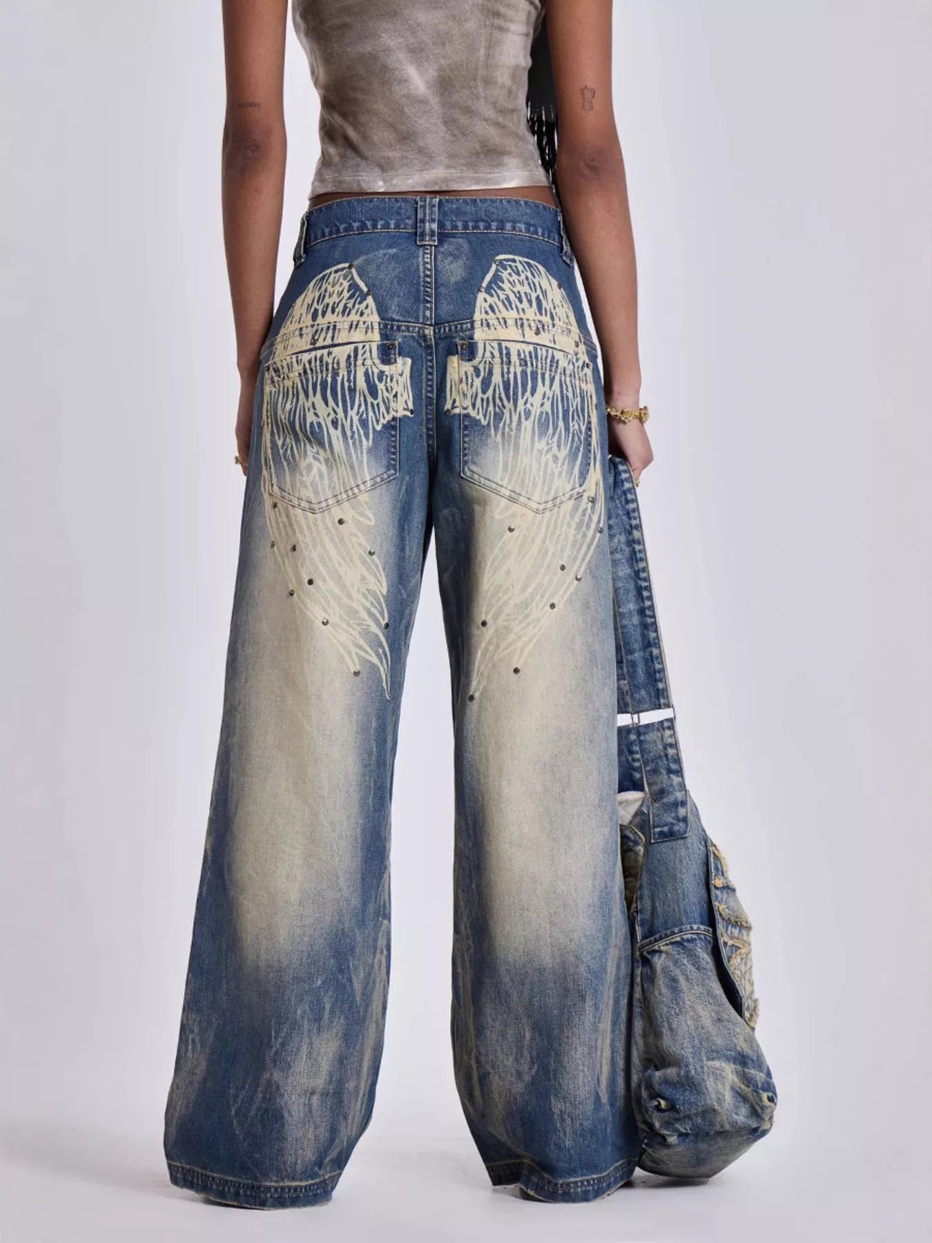 Person wearing wide-leg jeans with a unique design, holding another pair of jeans.