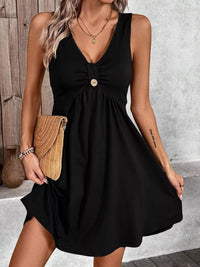 Woman wearing a black dress with a button detail, holding a beige clutch against a neutral background.
