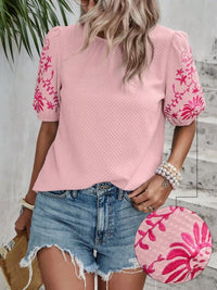 Woman wearing a pink blouse with floral patterns and denim shorts, holding a matching pink bag.