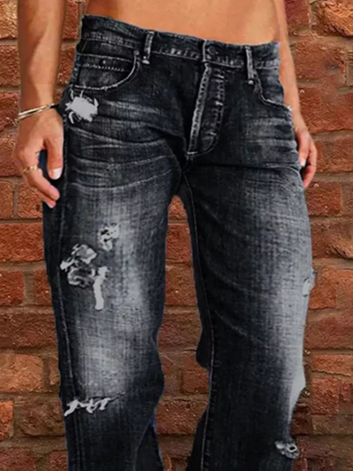 Person wearing distressed black jeans against a brick wall.