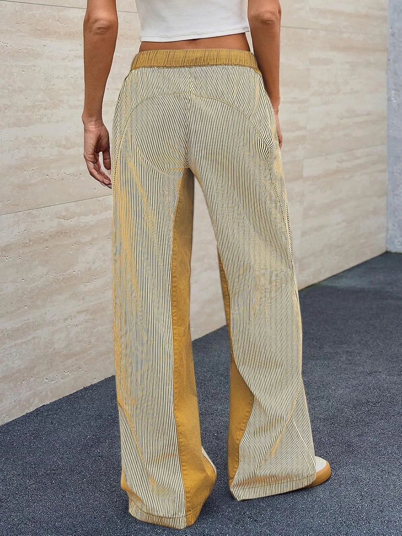 Person wearing mustard yellow and beige pleated pants against a neutral background