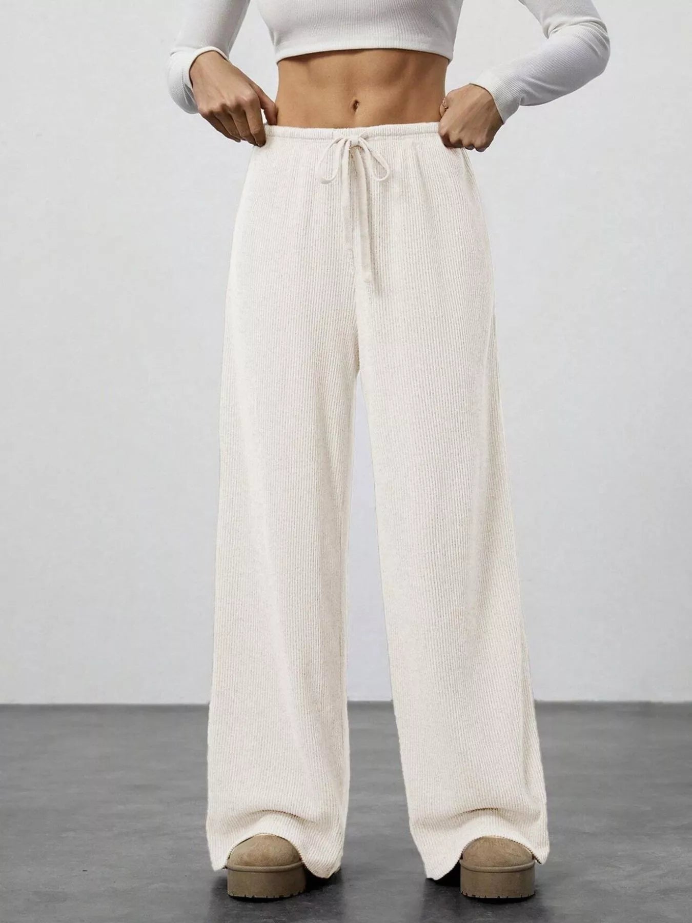 Person wearing white wide-leg pants and a white crop top on a plain background