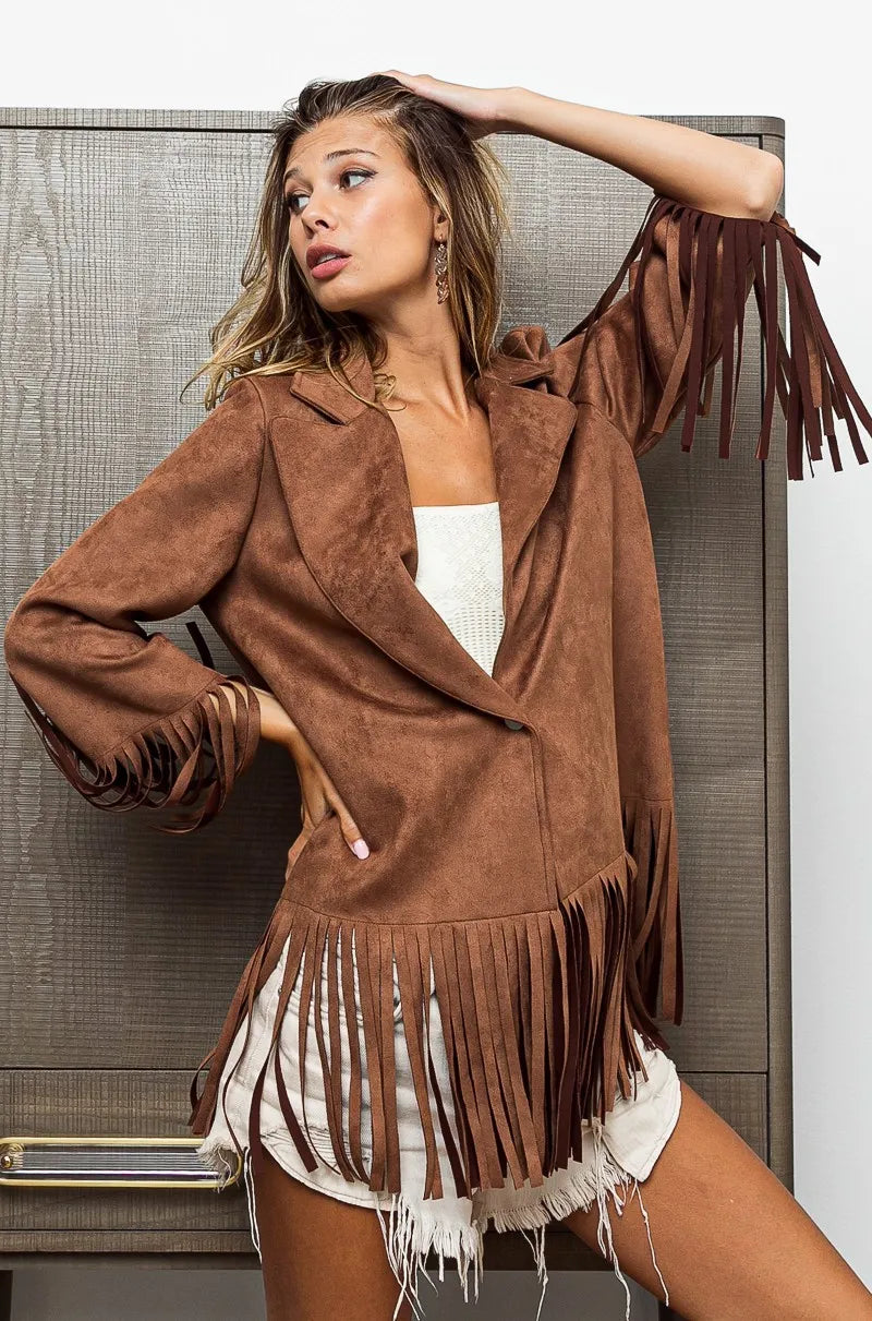 Woman wearing a brown suede jacket with fringe details against a neutral background