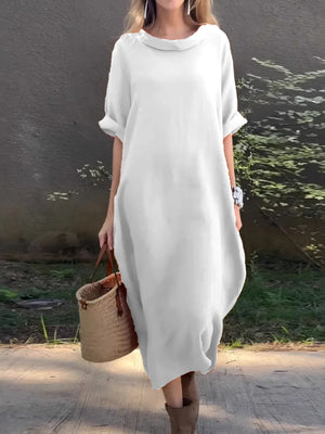 Woman wearing a white dress holding a woven bag outdoors.
