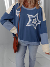 Person wearing a blue sweater with star designs, holding a brown bag against a neutral background