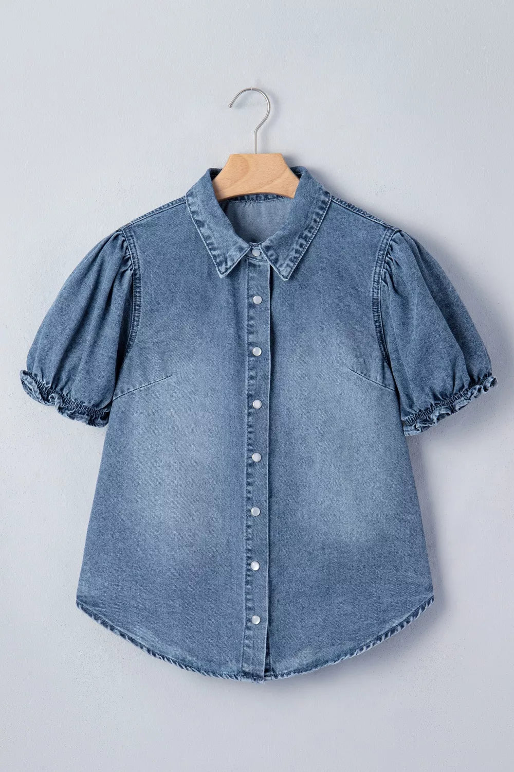 Blue denim shirt with puff sleeves on a hanger against a light gray background