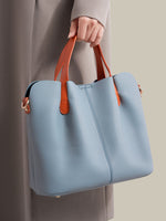 Blue handbag with brown handles held by a person wearing a long coat.