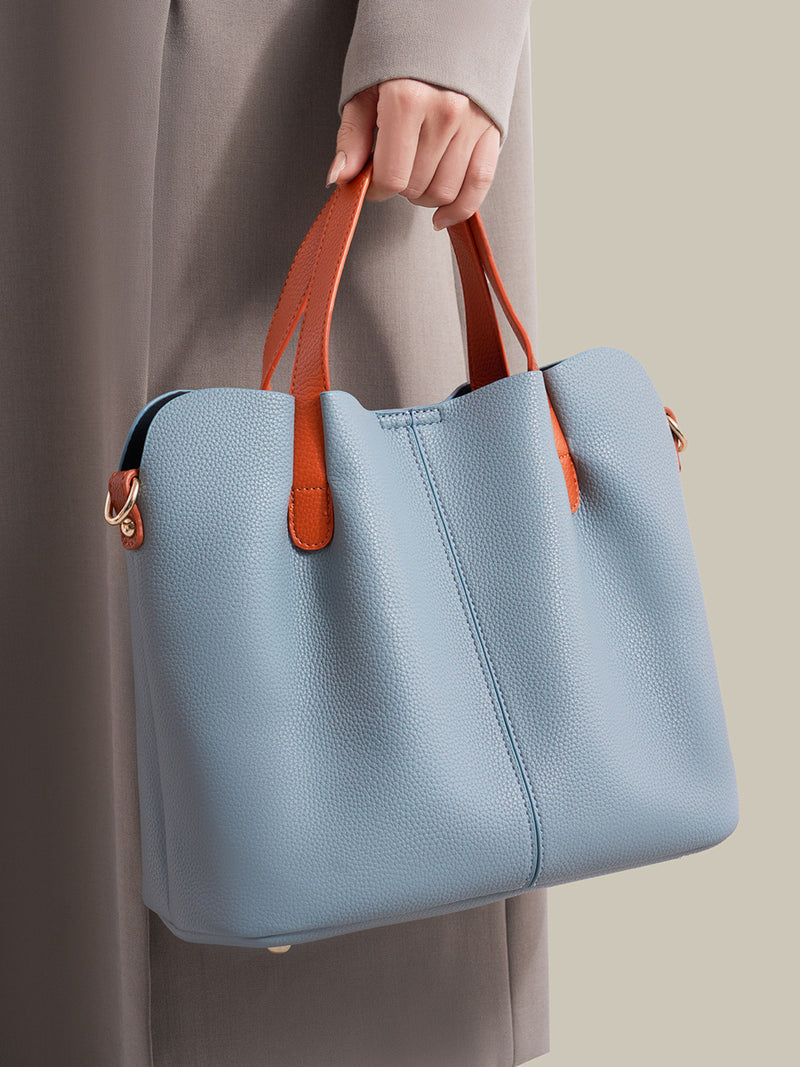 Blue handbag with brown handles held by a person wearing a long coat.