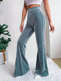 Teal flared pants worn by a person against a white wall.