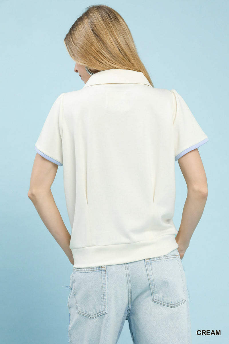 Woman wearing a cream-colored polo shirt with light blue trim on a light blue background