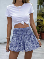 Person wearing a white tied crop top and blue floral shorts.