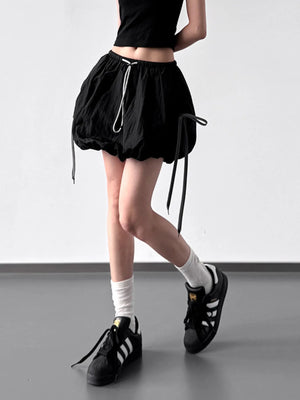 Person wearing black drawstring shorts, black top, white socks, and black Adidas shoes on a plain background