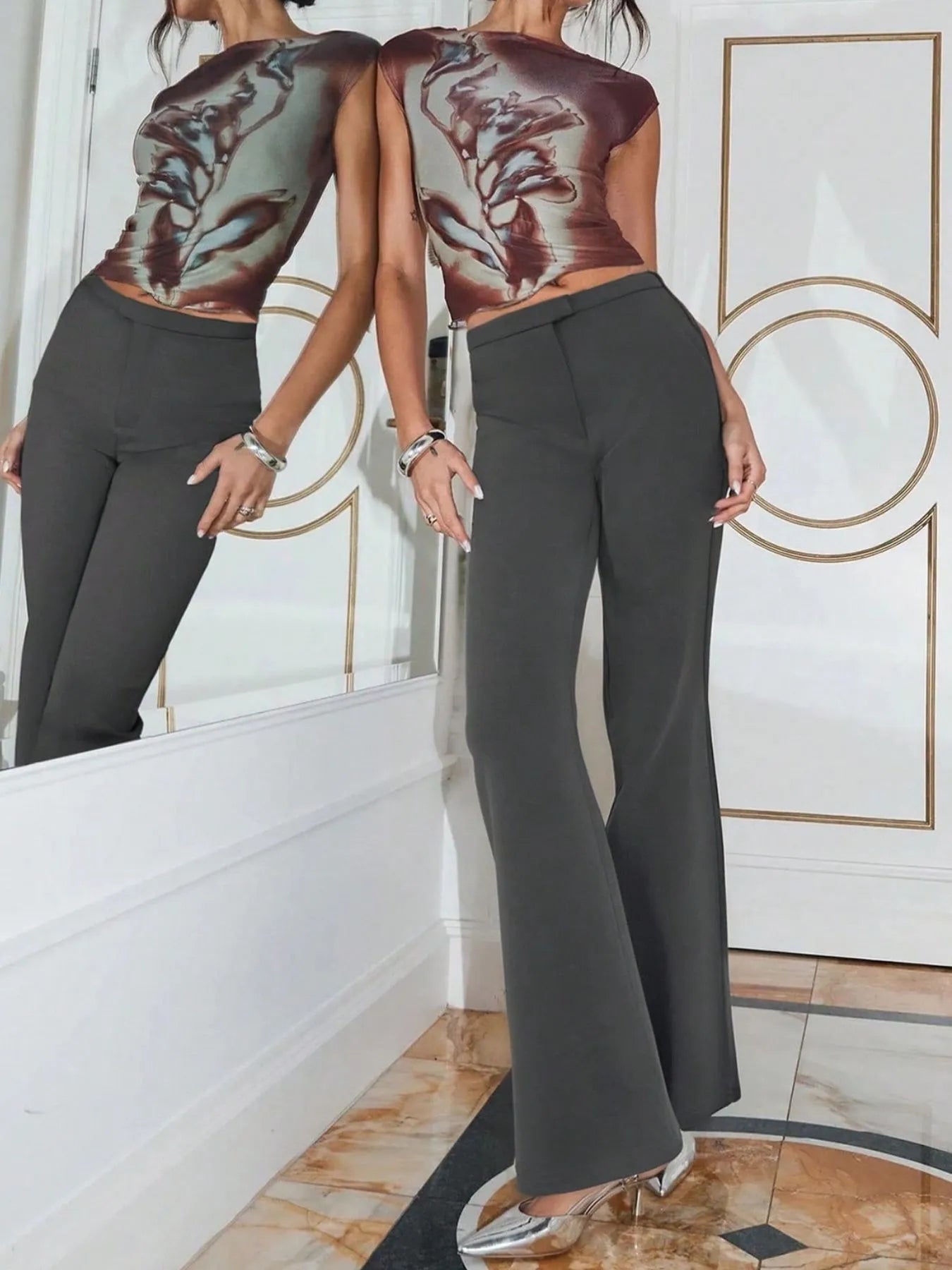 Person wearing a patterned top and dark pants standing in front of a mirror.