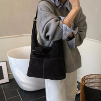 Person holding a black handbag with a neutral background