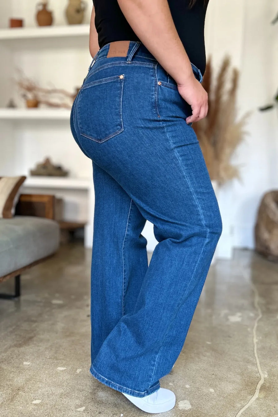 Person wearing blue jeans in a room with a white shelf and decorative items.