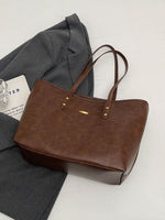 Brown leather tote bag on a light gray surface with a gray jacket and white paper underneath.
