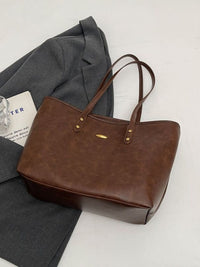 Brown leather tote bag on a light gray surface with a gray jacket and white paper underneath.