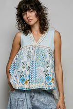 Woman wearing a sleeveless, patchwork-style top with floral and geometric patterns on a plain background.