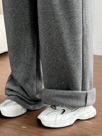 Gray sweatpants worn with white sneakers on a wooden floor.