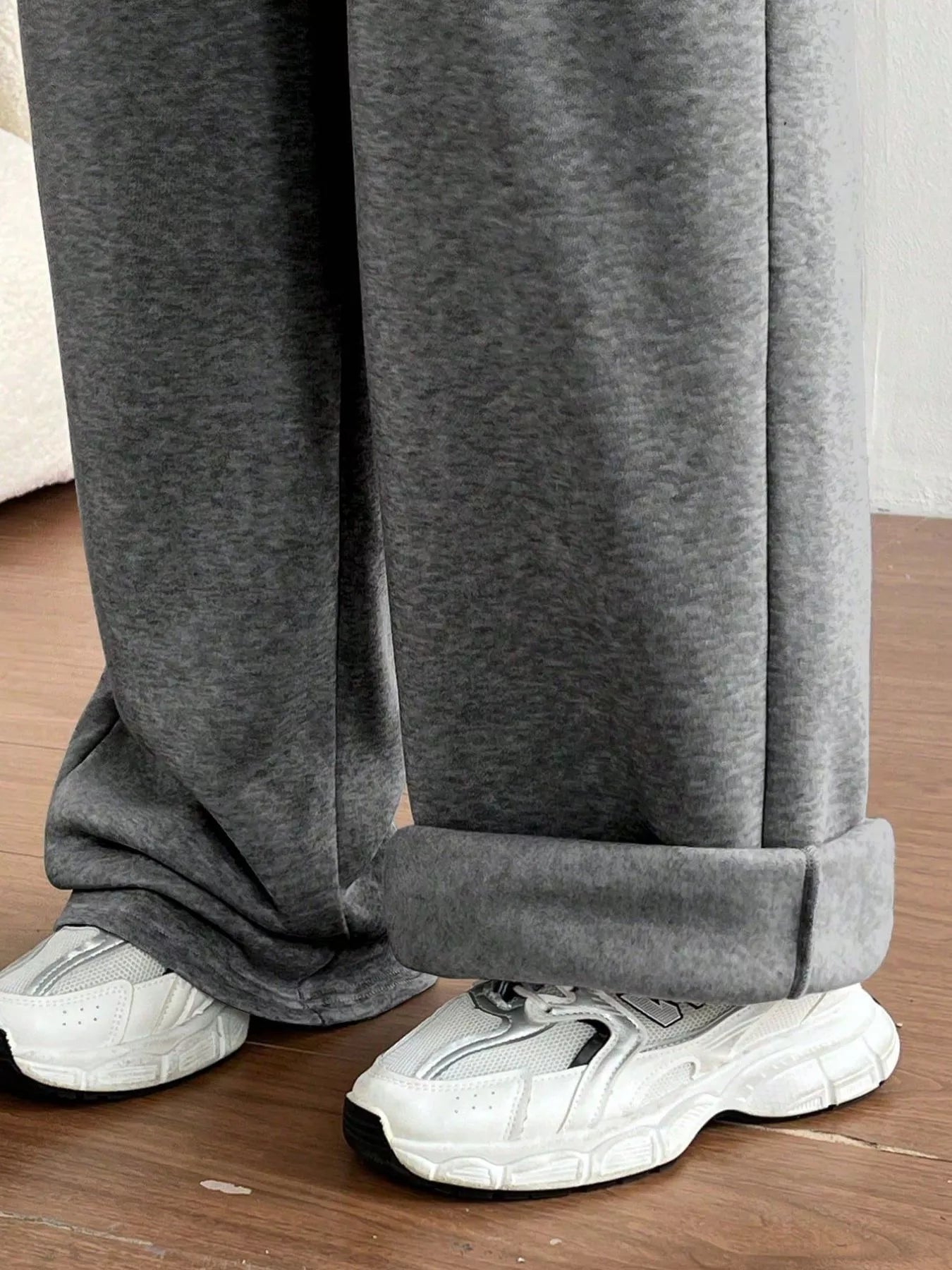 Gray sweatpants worn with white sneakers on a wooden floor.