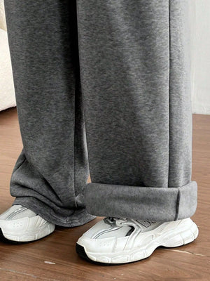 Gray sweatpants worn with white sneakers on a wooden floor.