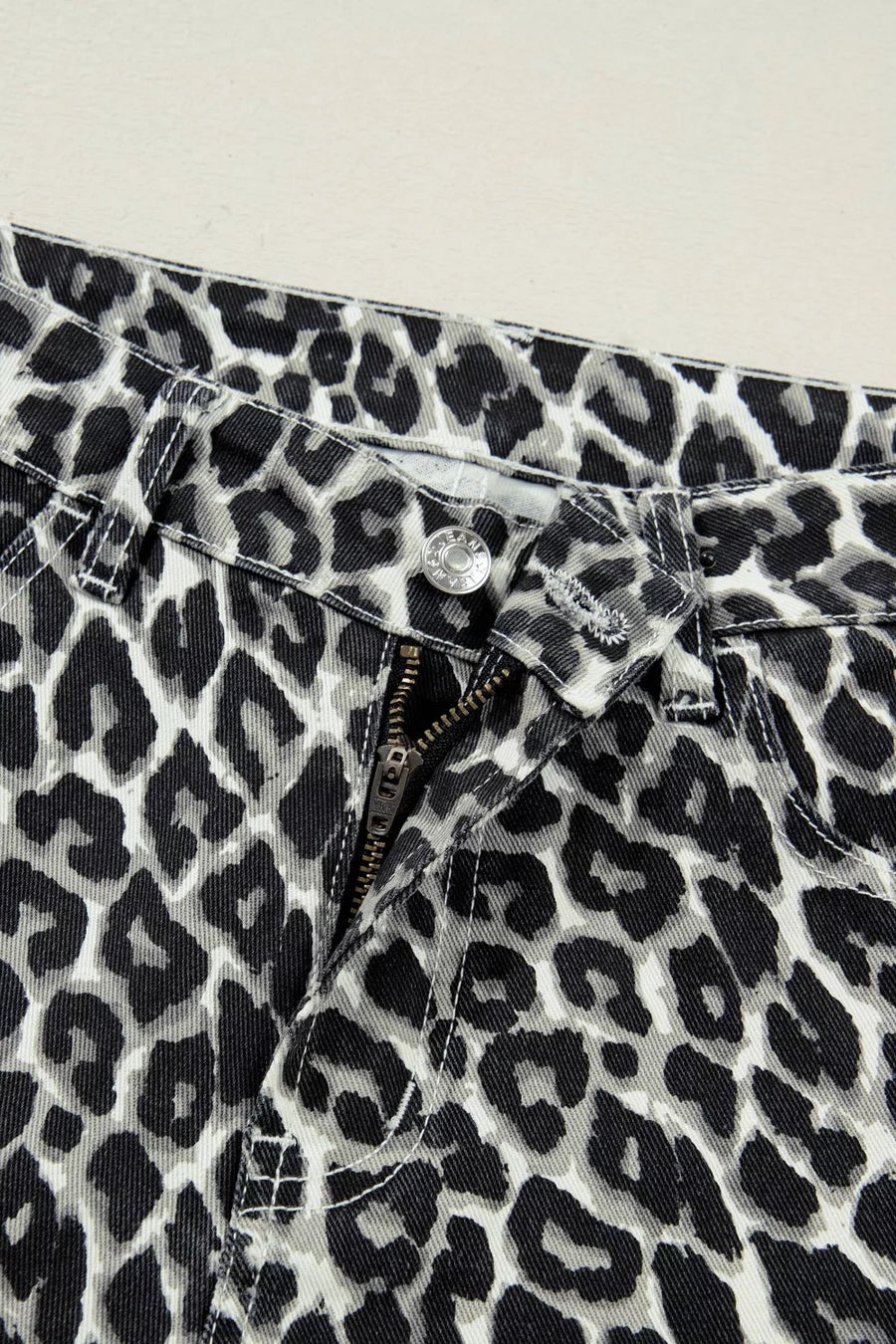 Close-up of leopard print pants with a button and zipper on a light background