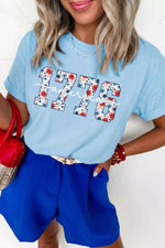 Woman wearing a light blue t-shirt with '1776' design, holding a red handbag.