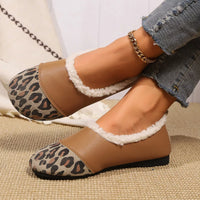 Brown slippers with leopard print accents worn by a person sitting on a textured surface.