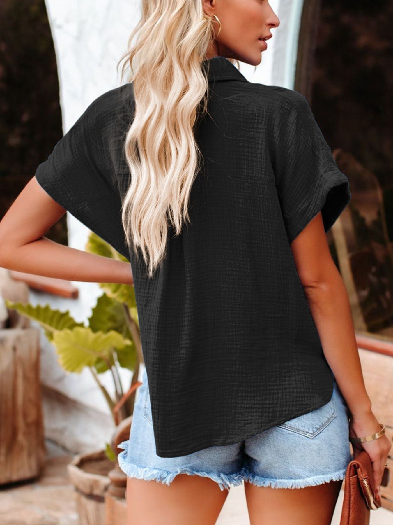 Woman wearing a black short-sleeve shirt and denim shorts outdoors.