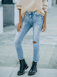 Person wearing distressed blue jeans and black boots on a blurred urban background