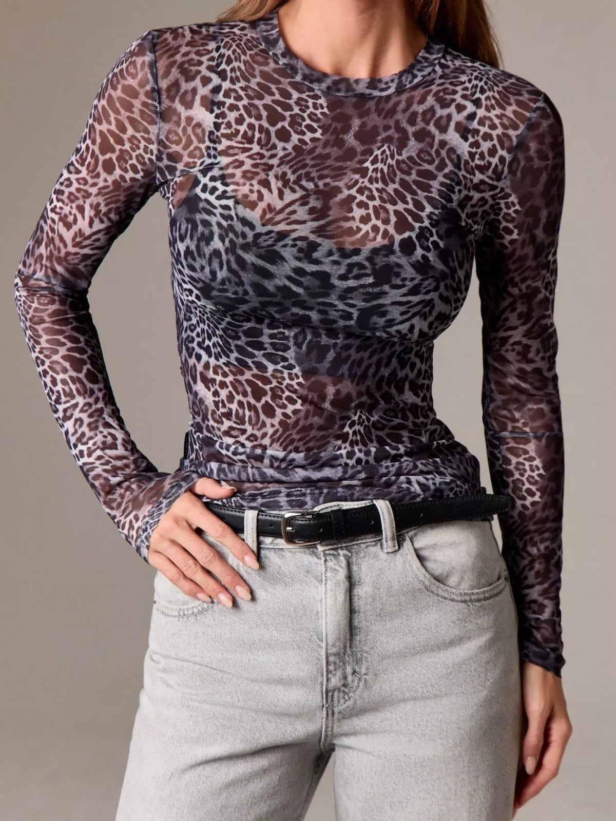 Person wearing a sheer leopard print long-sleeve top and light gray jeans on a neutral background