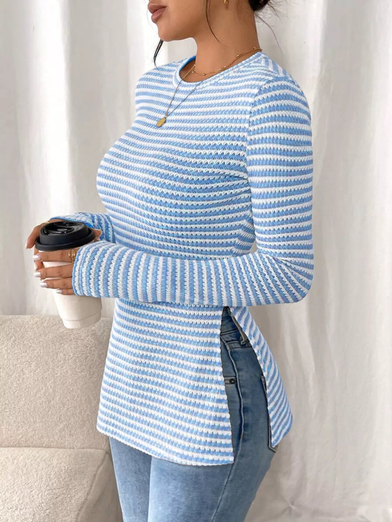 Person wearing a blue and white striped long-sleeve top holding a coffee cup.