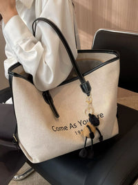 Beige handbag with black handle and decorative keychain on a car seat.