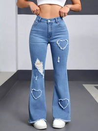 Person wearing blue flared jeans with heart-shaped holes on a plain background