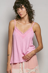 Woman wearing a pink lace-trimmed top against a plain background