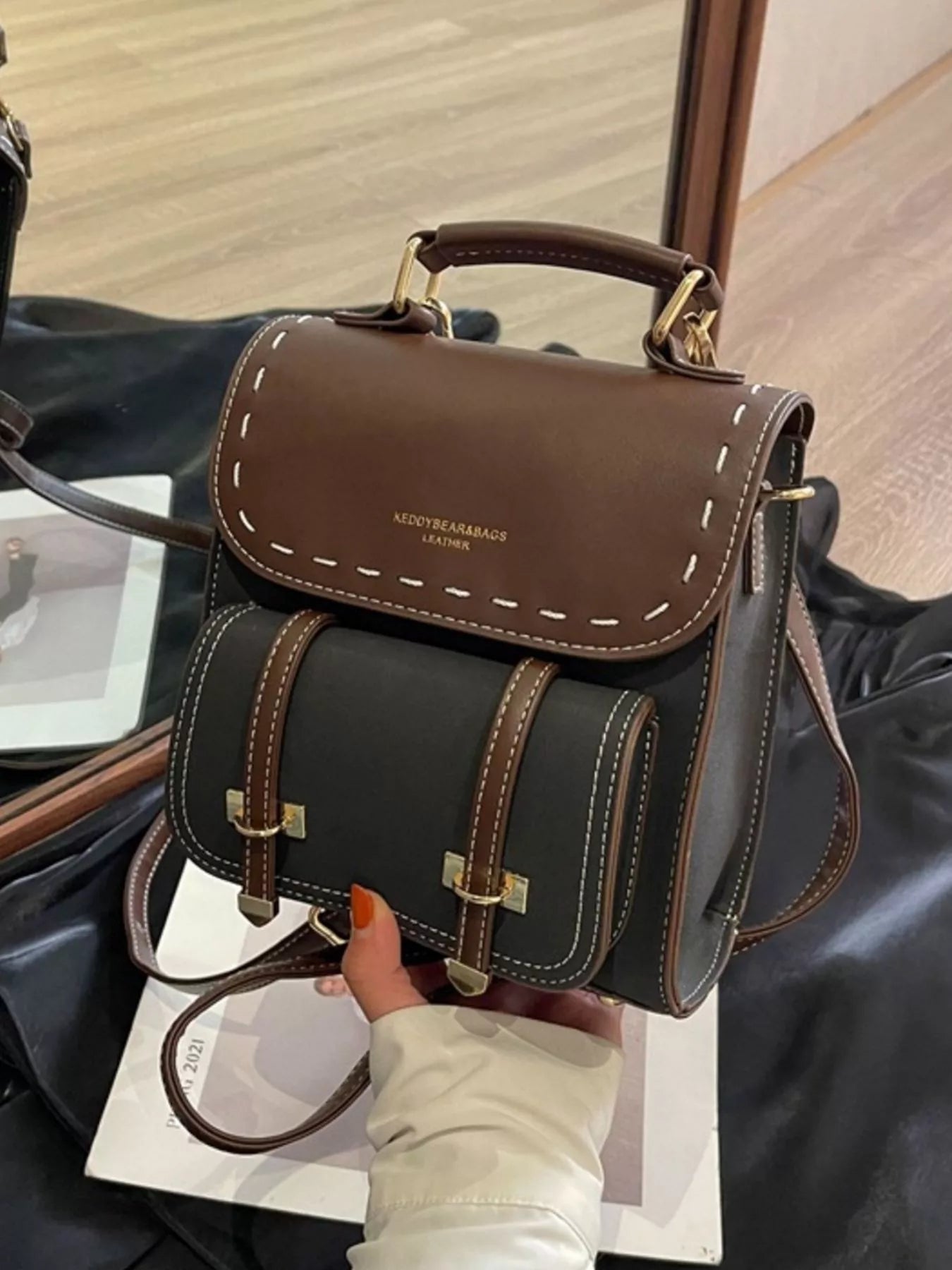 Brown and black leather handbag held by a person with a blurred background