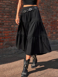 Person wearing a black tiered skirt with a belt and black boots against a brick wall.