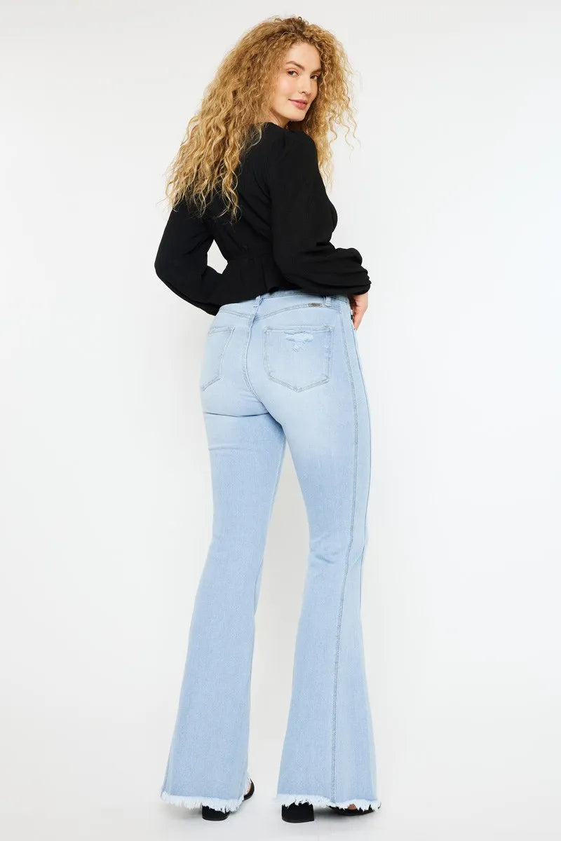 Woman wearing light blue flared jeans and a black top on a white background