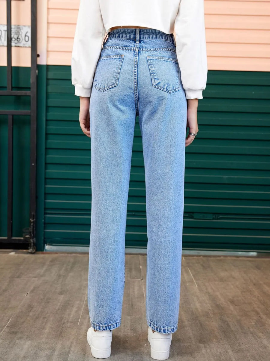 Person wearing light blue jeans standing in front of a green door.