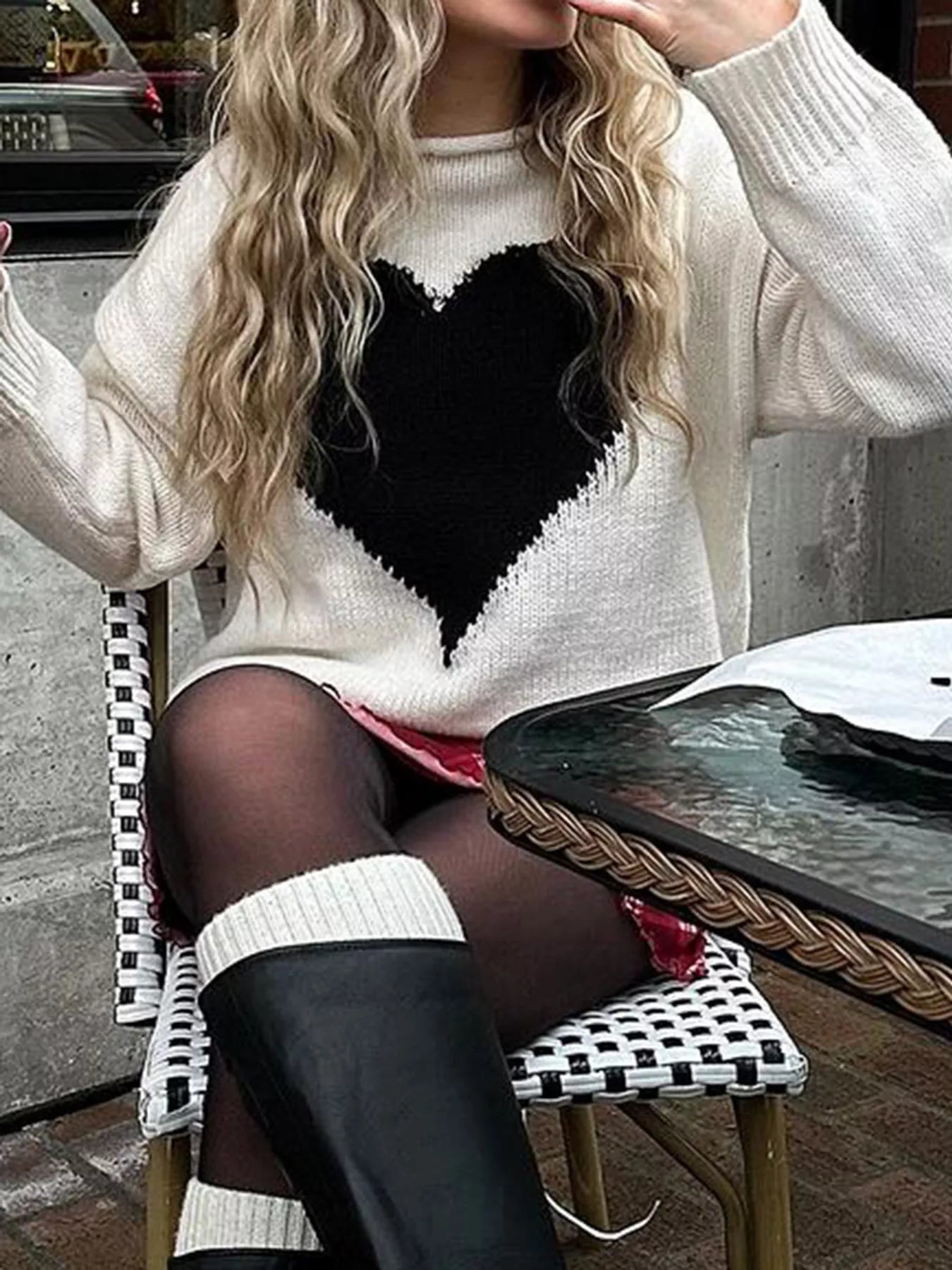 Person wearing a white sweater with a black heart design, sitting outdoors.