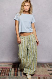 Woman wearing a light blue crop top and patterned pants against a plain background