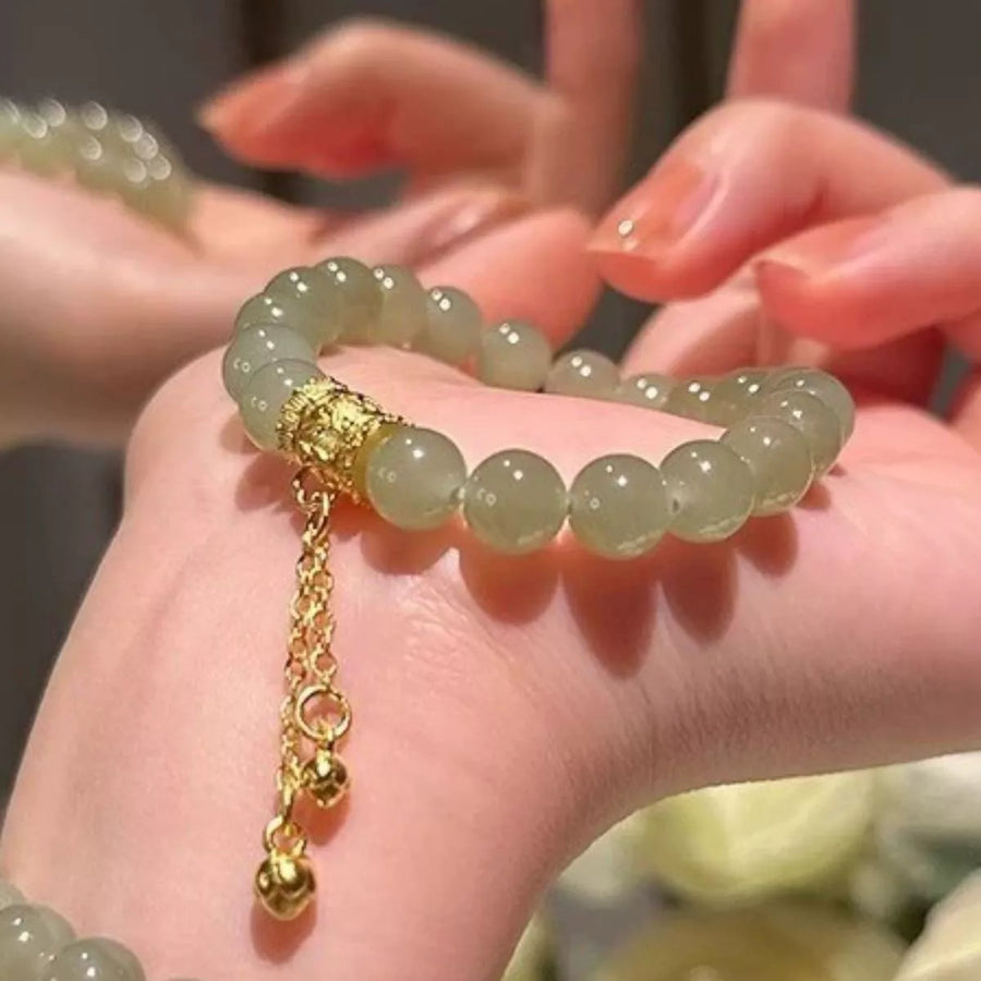 Close-up of a hand wearing a light green beaded bracelet with a gold chain.